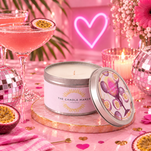 Load image into Gallery viewer, A pink-themed scented candle tin by The Candle Maker sits on a pink marble tray, styled with a matching lid, cocktail glasses, passion fruit, disco balls, and a glowing pink heart sign in the background.