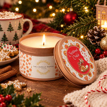 Load image into Gallery viewer, A lit candle in an open round tin with the lid leaning beside it on a wooden surface. The label reads 'The Candle Maker' and 'Christmas Coffee,' with a festive holiday scene including pine branches, ornaments, cookies, cinnamon sticks, and a mug in the background.
