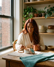 Load image into Gallery viewer, Woman sitting at a wooden table with a cup and Unstoppable Scented Candle
